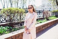 Young beautiful stylish girl walking and posing in white dress and pink coat in city . Outdoor summer portrait of young classy wom Royalty Free Stock Photo