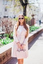 Young beautiful stylish girl walking and posing in white dress and pink coat in city . Outdoor summer portrait of young classy wom Royalty Free Stock Photo