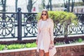 Young beautiful stylish girl walking and posing in white dress and pink coat in city . Outdoor summer portrait of young classy wom Royalty Free Stock Photo