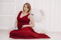 Young beautiful stylish pregnant woman in red long evening dress on white background of child room Royalty Free Stock Photo