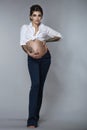 Young beautiful stylish tattooed pregnant woman with updo hair wearing trendy bell bottom navy blue pants and white tied up shirt Royalty Free Stock Photo