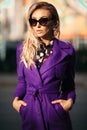 Young beautiful stylish woman in sunglasses and violet coat posing at street.