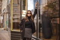 Young beautiful stylish woman in trendy clothes standing on empty city street and looking at camera