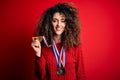 Young beautiful succesful woman with curly hair and piercing winning medals with a happy face standing and smiling with a