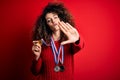 Young beautiful succesful woman with curly hair and piercing winning medals with open hand doing stop sign with serious and