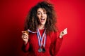 Young beautiful succesful woman with curly hair and piercing winning medals screaming proud and celebrating victory and success