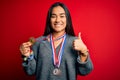 Young beautiful successful asian woman wearing medals standing over red background happy with big smile doing ok sign, thumb up Royalty Free Stock Photo