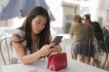 Young beautiful and sweet Asian Chinese woman sitting happy outdoors at street cafe using internet travel and social media app in Royalty Free Stock Photo