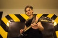 Young beautiful tattooed girl with a guitar, rock singer recording the sound in professional studio on the striped wall