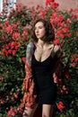 Young beautiful tattooed woman with closed eyes in rose garden. Outdoor portrait of a romantic girl with hard light