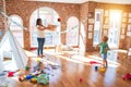Young beautiful teacher and toddler playing basketball using wicker basket and ball around lots of toys at kindergarten Royalty Free Stock Photo