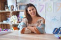 Young beautiful teacher woman wearing sweater and glasses sitting on desk at kindergarten happy face smiling with crossed arms Royalty Free Stock Photo