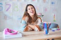 Young beautiful teacher woman wearing sweater and glasses sitting on desk at kindergarten happy face smiling with crossed arms Royalty Free Stock Photo