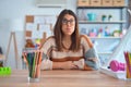 Young beautiful teacher woman wearing sweater and glasses sitting on desk at kindergarten puffing cheeks with funny face Royalty Free Stock Photo