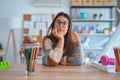 Young beautiful teacher woman wearing sweater and glasses sitting on desk at kindergarten thinking looking tired and bored with