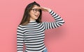 Young beautiful teen girl wearing casual clothes and glasses very happy and smiling looking far away with hand over head Royalty Free Stock Photo