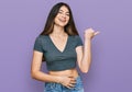 Young beautiful teen girl wearing casual crop top t shirt smiling with happy face looking and pointing to the side with thumb up Royalty Free Stock Photo