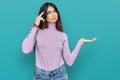 Young beautiful teen girl wearing turtleneck sweater confused and annoyed with open palm showing copy space and pointing finger to Royalty Free Stock Photo