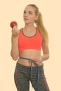 Young beautiful teenage girl holding red apple while thinking and measuring waist ready for gym Royalty Free Stock Photo