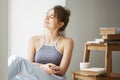 Young beautiful teenage girl holding smart phone smiling with closed eyes sitting on floor among old books near window Royalty Free Stock Photo