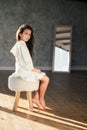 Young beautiful teenage girl sitting on the chair near mirror with sad emotions. Caucasian child in white dress Royalty Free Stock Photo