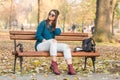 Young beautiful teenage girl sitting smiling ripped jeans black hat autumn park bench Royalty Free Stock Photo