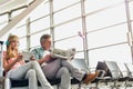 Young beautiful teenage girl watching movie on digital tablet with headphones on while her father is reading newspaper in airport Royalty Free Stock Photo