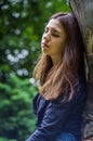 Young beautiful teenager girl with long hair in a shirt and denim shorts resting on a tree during a walk in the park Striysky in Royalty Free Stock Photo