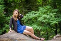 Young beautiful teenager girl with long hair in a shirt and denim shorts resting on a tree during a walk in the park Striysky in Royalty Free Stock Photo