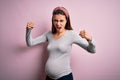 Young beautiful teenager girl pregnant expecting baby over isolated pink background angry and mad raising fists frustrated and