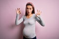 Young beautiful teenager girl pregnant expecting baby over isolated pink background looking surprised and shocked doing ok Royalty Free Stock Photo