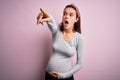 Young beautiful teenager girl pregnant expecting baby over isolated pink background Pointing with finger surprised ahead, open Royalty Free Stock Photo