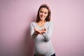 Young beautiful teenager girl pregnant expecting baby over isolated pink background Smiling with hands palms together receiving or Royalty Free Stock Photo