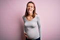 Young beautiful teenager girl pregnant expecting baby over isolated pink background sticking tongue out happy with funny Royalty Free Stock Photo