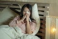 Young beautiful tired and ill Asian Japanese woman lying on bed at home sick suffering cold flu and temperature feeling unwell and Royalty Free Stock Photo