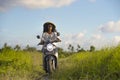 Young beautiful tourist or nomad traveler black afro American woman riding motorbike in tropical field wearing traditional Asian h