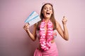 Young beautiful tourist woman on vacation wearing bikini and hawaiian lei holding boarding pass screaming proud and celebrating Royalty Free Stock Photo