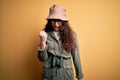 Young beautiful tourist woman on vacation wearing explorer hat and binoculars angry and mad raising fist frustrated and furious Royalty Free Stock Photo