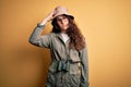 Young beautiful tourist woman on vacation wearing explorer hat and binoculars confuse and wonder about question