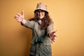 Young beautiful tourist woman on vacation wearing explorer hat and binoculars looking at the camera smiling with open arms for hug Royalty Free Stock Photo