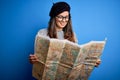 Young beautiful tourist woman on vacation wearing glasses and beret holding city map with a happy face standing and smiling with a Royalty Free Stock Photo