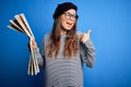 Young beautiful tourist woman on vacation wearing glasses and beret holding city map pointing and showing with thumb up to the Royalty Free Stock Photo