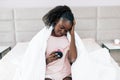 Young beautiful unhappy sad woman with alarm clock is sitting on the bed Royalty Free Stock Photo