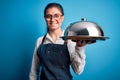 Young beautiful waitress woman with blue eyes holding tray with dome over isolated background with a happy face standing and