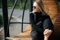 Young beautiful white girl is sitting on a park bench.Cute female lifestyle, portrait with soft focus.Thoughtful stylish