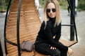 Young beautiful white girl is sitting on a park bench.Cute female lifestyle, portrait with soft focus.Thoughtful stylish