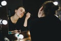 Young beautiful woman applying her make up face with brush, looking in a mirror, sitting on chair at dressing room with Royalty Free Stock Photo