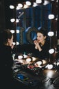 Young beautiful woman applying her make-up lips, looking in a mirror, sitting on chair at Theatre dressing room with Royalty Free Stock Photo