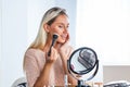 Young beautiful woman applying her make-up, looking in a mirror. Beautiful girl with cosmetic powder brush for make up. Makeup. Royalty Free Stock Photo