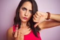 Young beautiful woman applying red lipstick over pink isolated background with angry face, negative sign showing dislike with Royalty Free Stock Photo